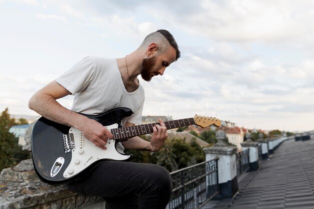 Vista lateral del artista masculino en la azotea tocando la guitarra eléctrica