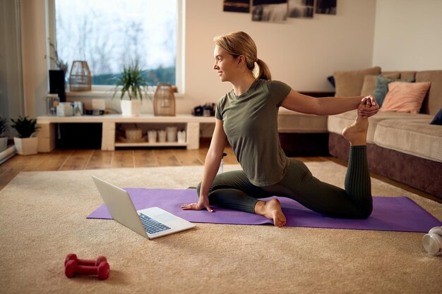 Vista lateral de la atleta femenina haciendo ejercicio de relajación de yoga en la sala de estar