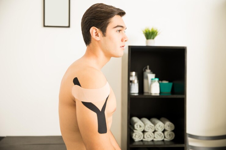 Foto gratuito vista lateral del atleta masculino sin camisa con cinta de kinesiología en el hombro en la clínica
