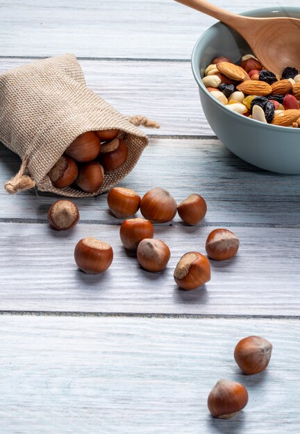 Vista lateral de avellanas esparcidas de un saco y un tazón con nueces se mezclan en madera rústica