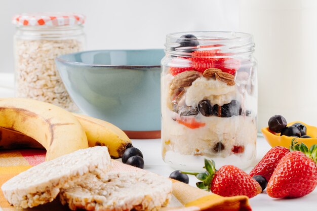 Vista lateral de avena durante la noche con fresas frescas, arándanos y nueces en un frasco de vidrio en la mesa rústica