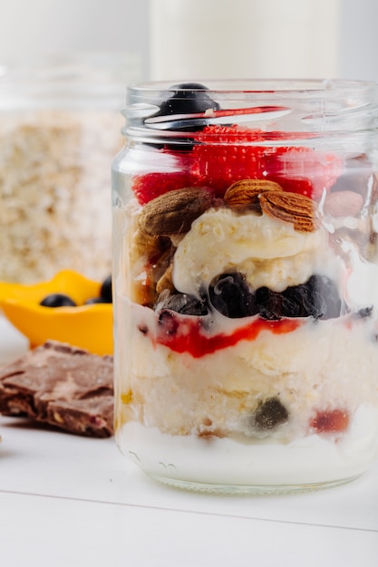 Vista lateral de avena durante la noche con fresas frescas, arándanos y nueces en un frasco de vidrio en la mesa rústica