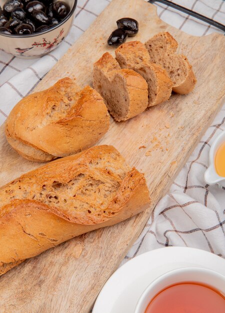 Vista lateral de baguette negro cortado y en rodajas con una taza de mantequilla de té sobre tela escocesa