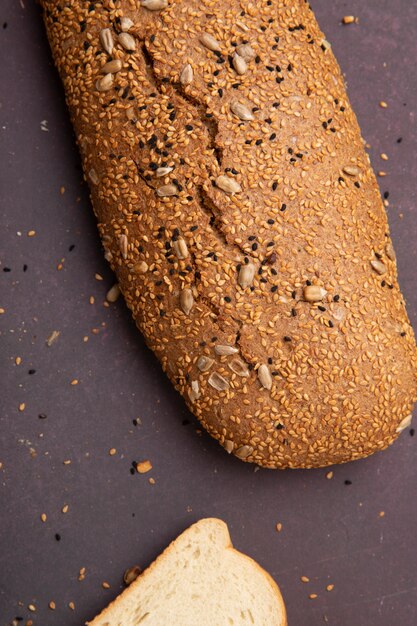 Vista lateral de baguette sin semillas con rebanada de pan blanco sobre fondo marrón con espacio de copia