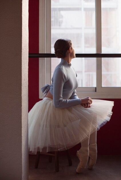 Vista lateral de la bailarina en falda tutú junto a la ventana