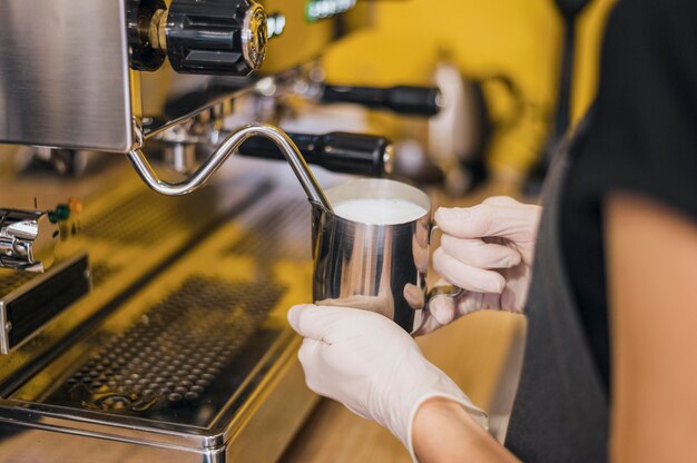 Vista lateral de barista con guantes de látex espumantes de leche