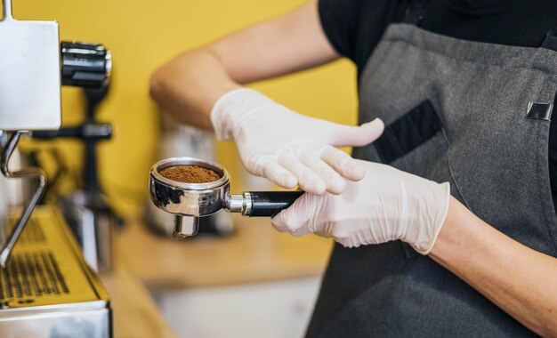 Vista lateral del barista con guantes de látex preparando café para máquina