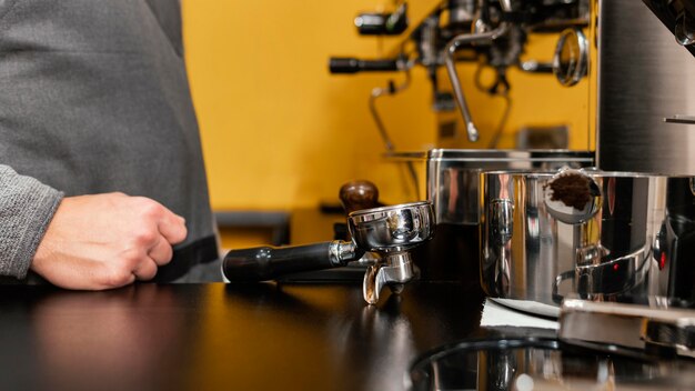 Vista lateral del barista masculino con delantal junto a la máquina de café