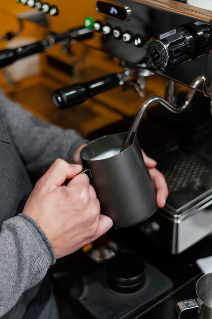 Vista lateral del barista masculino preparando espuma de leche para café