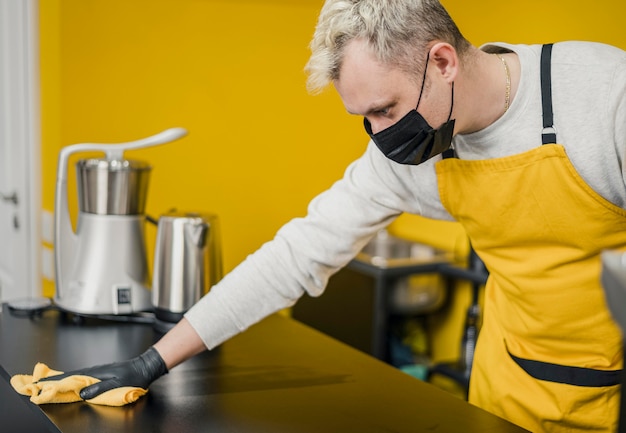 Vista lateral del barista masculino con superficie de mesa de limpieza de máscara médica