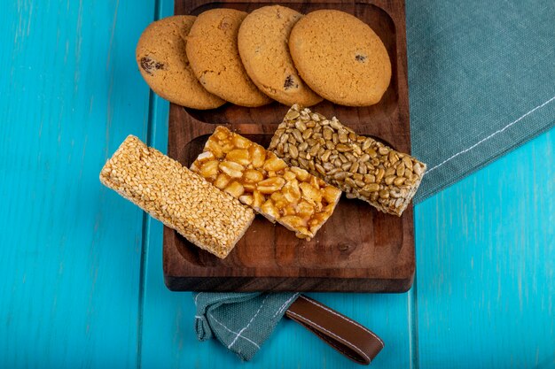 Vista lateral de barras de miel con semillas de maní, sésamo y girasol con galletas de avena en una tabla de madera