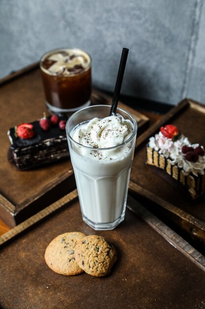 Vista lateral batido con crema batida en un vaso con galletas en una bandeja