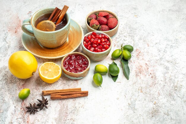 Vista lateral de bayas y té, una taza de té negro, frutas cítricas, mermelada, galletas de chocolate y canela.