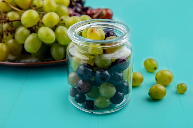Foto gratuito vista lateral de las bayas de uva en frasco y las uvas en plato sobre fondo azul