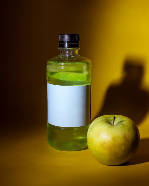 Vista lateral de la bebida de desintoxicación verde en botella con manzana sobre la mesa en amarillo oscuro
