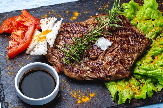 Vista lateral bistec a la parrilla carne roja con lechuga romero tomate y salsa de granada en una bandeja