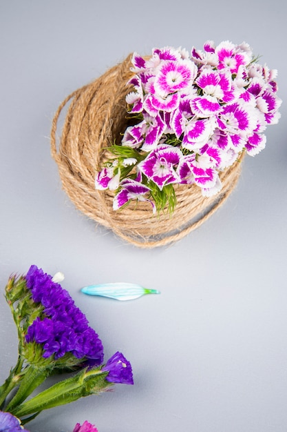 Vista lateral de una bola de cuerda con clavel turco de color púrpura y flores statice en mesa blanca