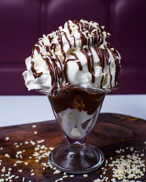 Foto gratuita vista lateral de bolas de helado blanco cubiertas con chocolate y nueces en un jarrón sobre una mesa de madera