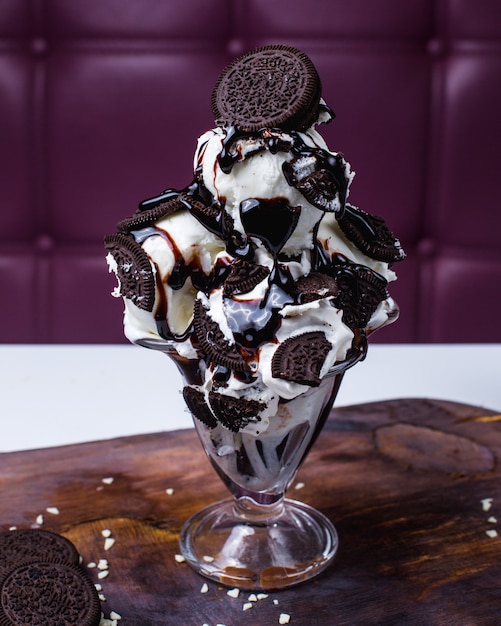 Foto gratuita vista lateral de bolas de helado blanco decoradas con galletas de chocolate y jarabe en un jarrón sobre una mesa de madera