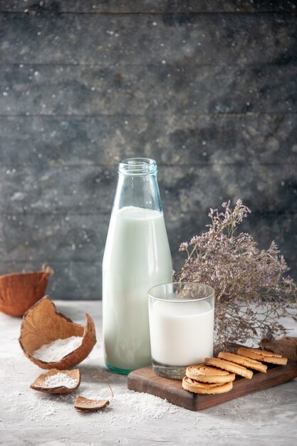 Vista lateral de la botella de vidrio y la taza llena de leche en la bandeja de madera flor en la pared oscura