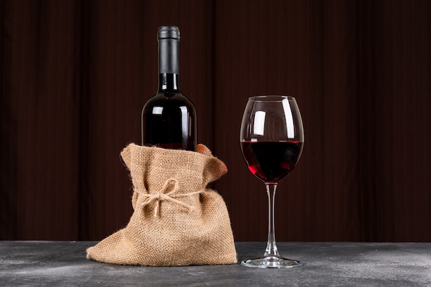 Vista lateral botella de vino tinto en bolsa de tela de saco en la mesa oscura y horizontal
