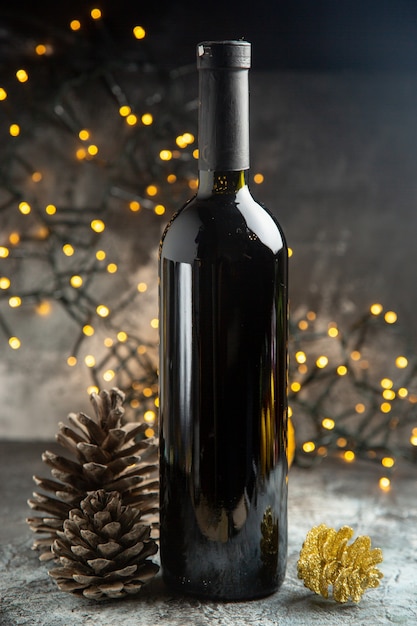 Vista lateral de la botella de vino tinto para la celebración y dos conos de coníferas sobre fondo oscuro
