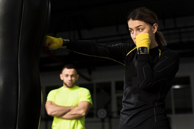 Vista lateral de la boxeadora con guantes de protección perforando saco pesado