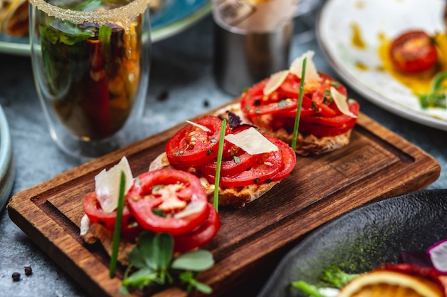 Vista lateral bruschetta con tomate albahaca cebolleta y parmesano en un tablero