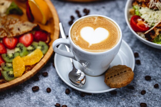 Vista lateral de café con leche con galletas de chocolate y granos de café sobre la mesa