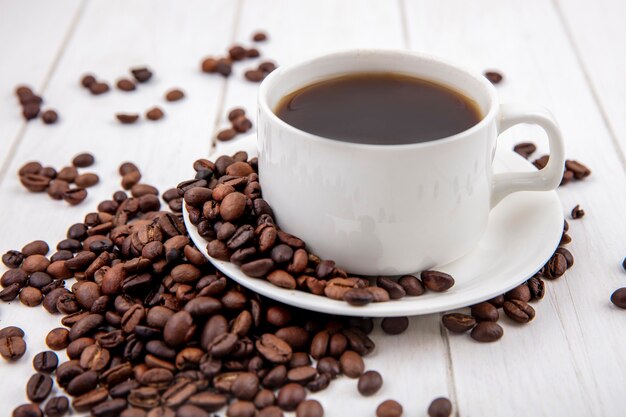 Vista lateral del café en una taza blanca con granos de café aislado sobre un fondo blanco de madera