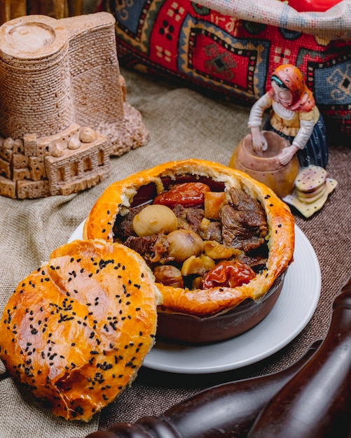 Vista lateral de carne al horno con castañas y frutas secas en una olla con masa encima cocida en el horno