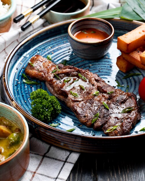 Vista lateral de carne asada con salsa picante y tomate a la parrilla con palitos de pan frito en un plato