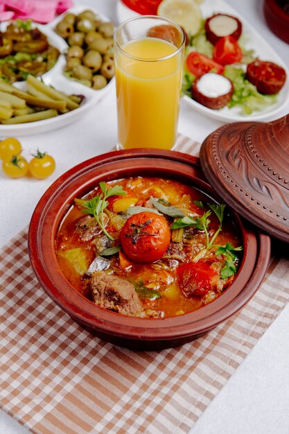 Vista lateral de carne guisada con papas y tomates en una olla de barro