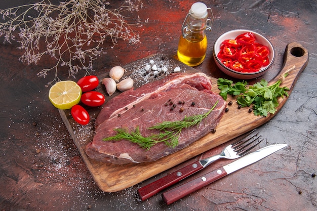 Vista lateral de la carne roja sobre la tabla de cortar de madera y ajo verde limón pimiento picado botella de aceite de tomate sobre fondo oscuro