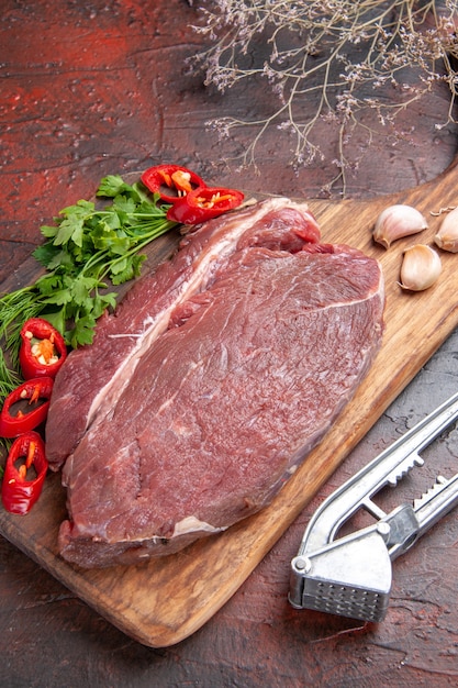 Vista lateral de la carne roja en la tabla de cortar de madera y ajo pimiento verde picado sobre fondo oscuro
