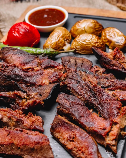 Vista lateral de carnes a la brasa con patatas y verduras a la plancha con salsas