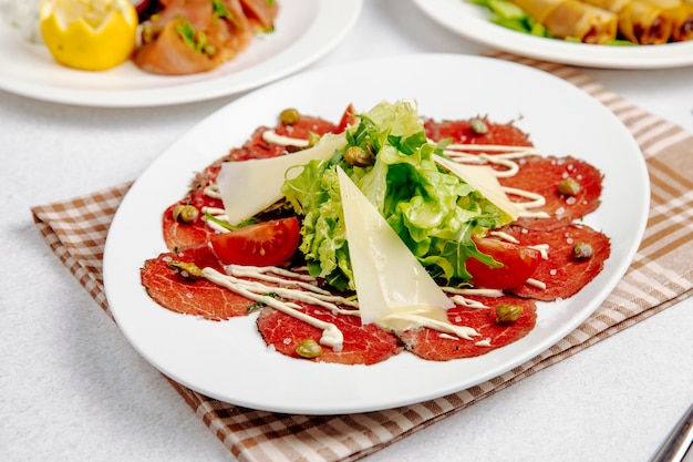 Vista lateral de carpaccio de ternera con rúcula de parmesano y tomates