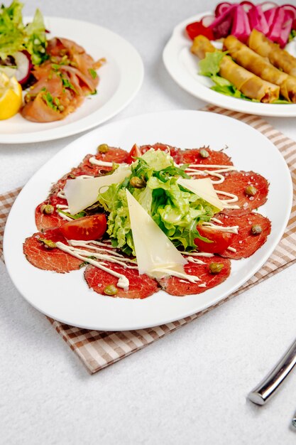 Vista lateral de carpaccio de ternera con rúcula de parmesano y tomates