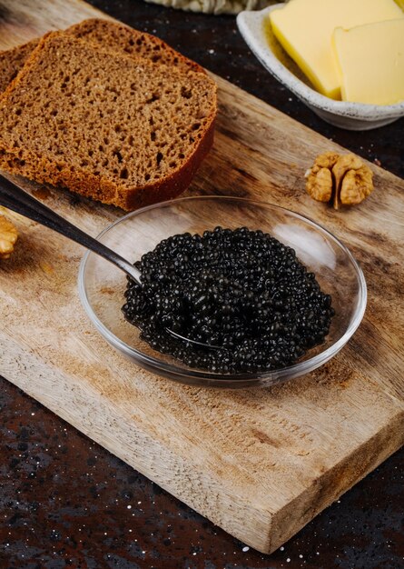 Vista lateral de caviar negro con mantequilla de pan de centeno y nueces en un tablero
