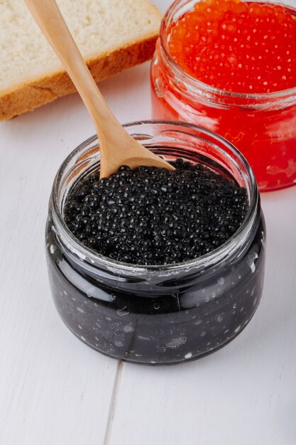 Vista lateral de caviar negro y rojo en frascos de vidrio con una cuchara