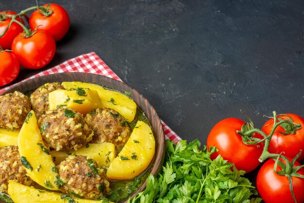 Vista lateral de una cena sabrosa con albóndigas, papas verdes en un tazón marrón sobre tomates de toalla pelados rojos sobre fondo negro con espacio libre