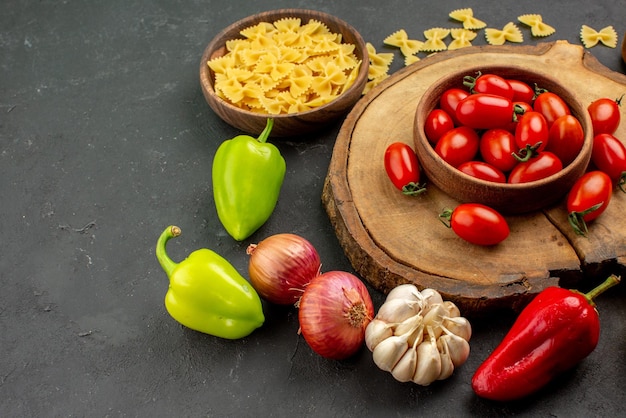 Foto gratuita vista lateral de cerca comida sabrosa pasta con ajo, cebolla y pimiento junto al tazón de tomates en la tabla de cortar de madera