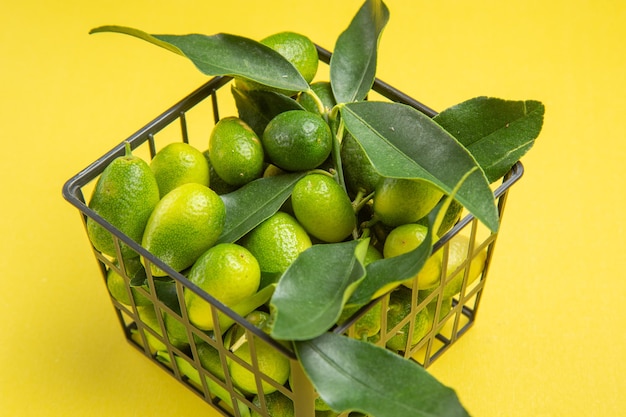 Vista lateral de cerca frutas con hojas frutos verdes con hojas en la canasta gris