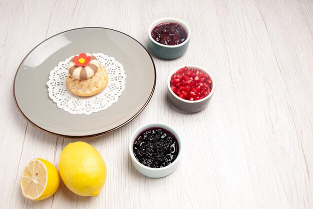 Vista lateral de cerca mermelada y cupcakes apetitosos cupcakes en el tapete de encaje junto a los cuencos de mermeladas de granada y limón sobre la mesa