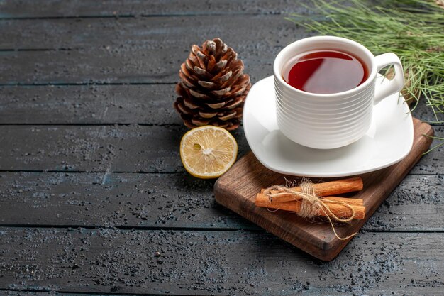 Vista lateral de cerca una taza de té una taza de té junto a los conos de limón, palitos de canela y ramas de los árboles de Navidad