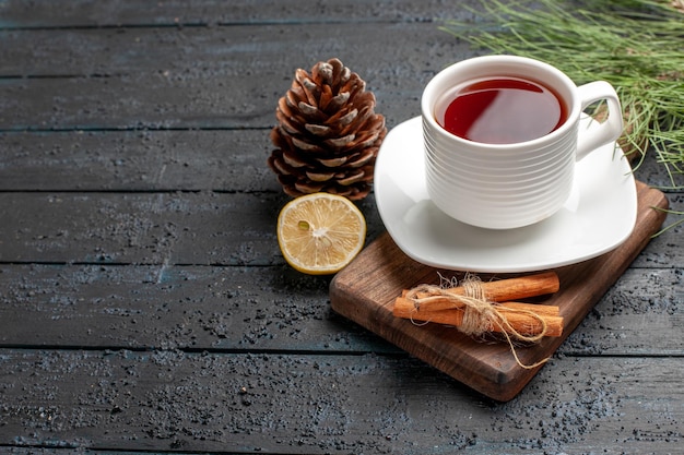 Vista lateral de cerca una taza de té una taza de té junto a los conos de limón, palitos de canela y ramas de los árboles de Navidad