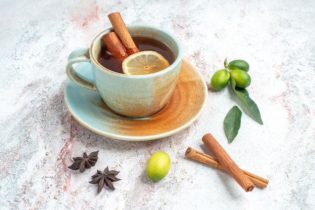 Vista lateral de cerca una taza de té una taza de té con limón y canela en el platillo con cítricos anís estrellado y palitos de canela sobre la mesa