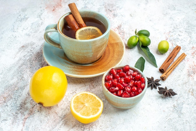 Vista lateral de cerca una taza de té una taza de té con limón y canela en el platillo junto a las semillas de limón de anís estrellado de granada y palitos de canela en la mesa