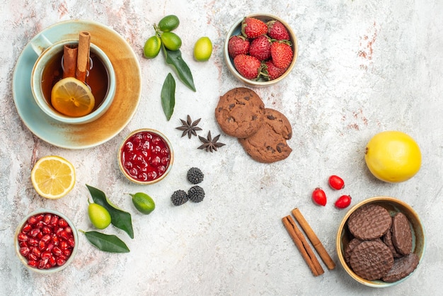 Vista lateral de cerca té con bayas galletas de chocolate la taza de té con limón y palitos de canela cuencos de bayas cítricos anís estrellado sobre la mesa