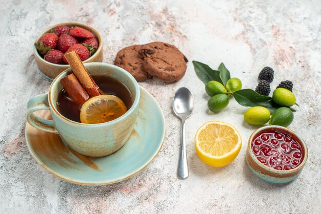 Foto gratuita vista lateral cercana bayas cuencos de bayas galletas de chocolate frutas cítricas granada limón cuchara una taza de té con limón sobre la mesa